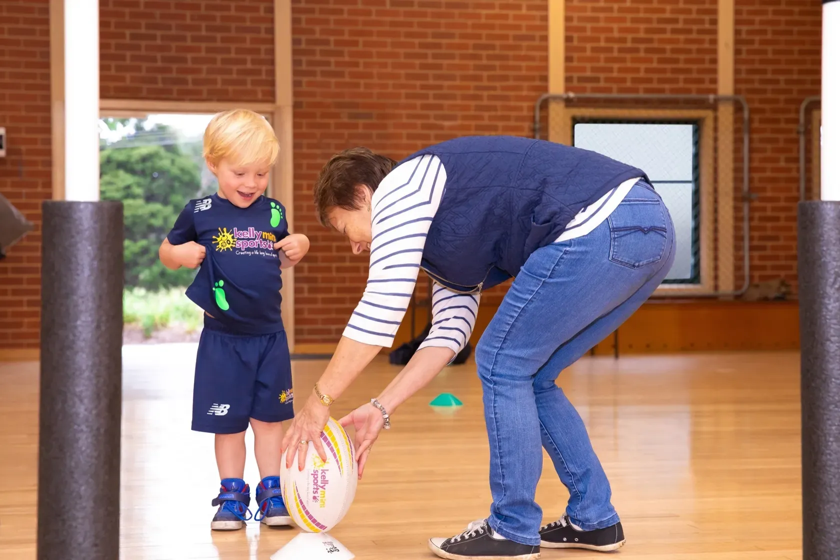Adult and child setting a rugby ball upright in a gymnasium