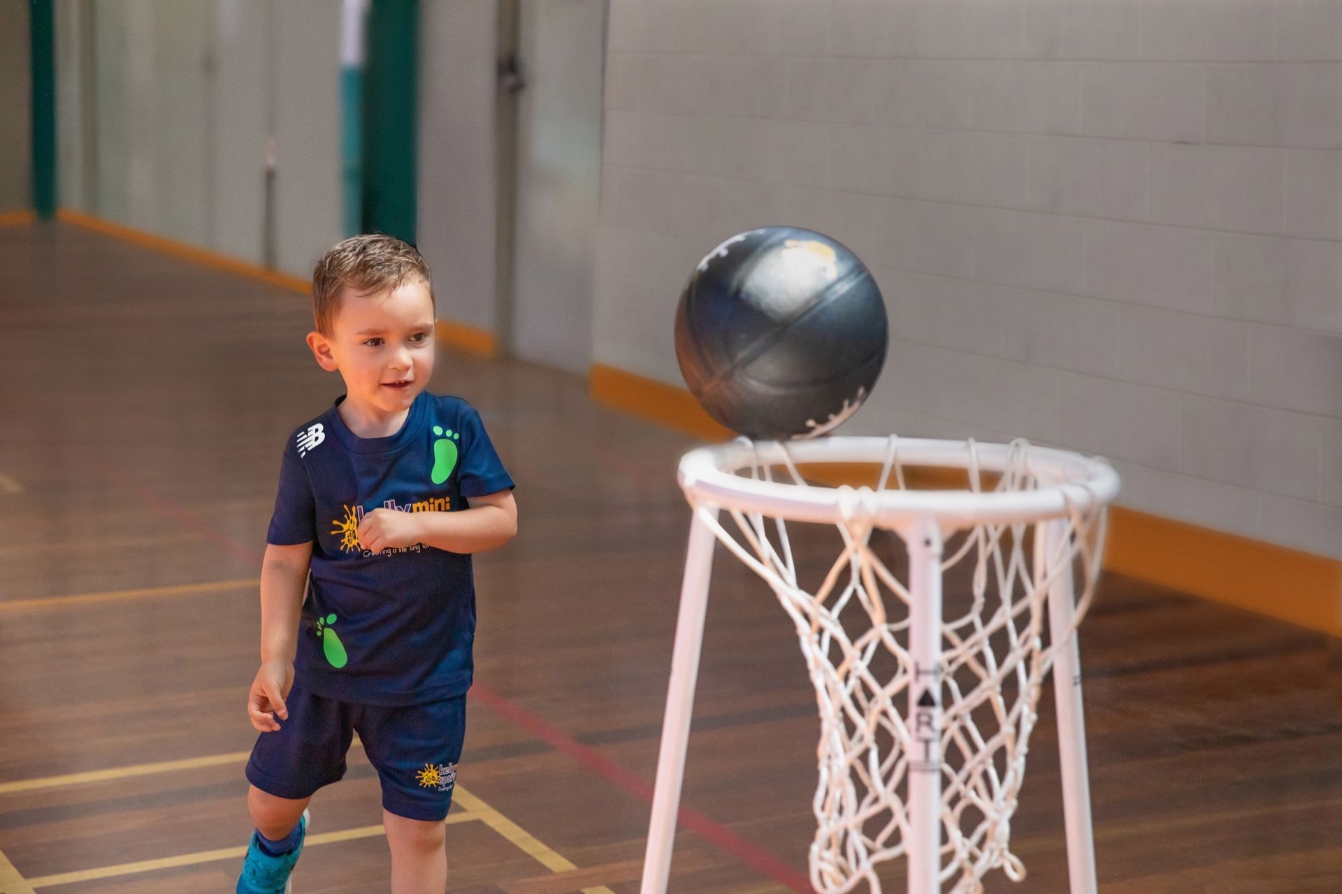 Child in a gym watching a basketball roll off a white net hoop