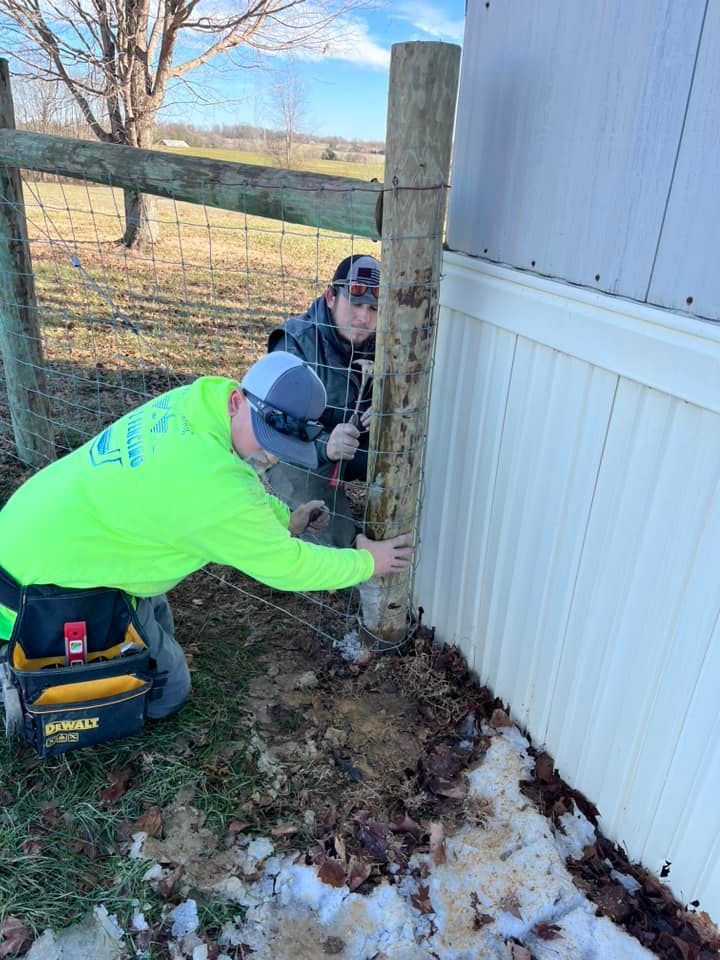 Two men are working on a fence post in the snow.
