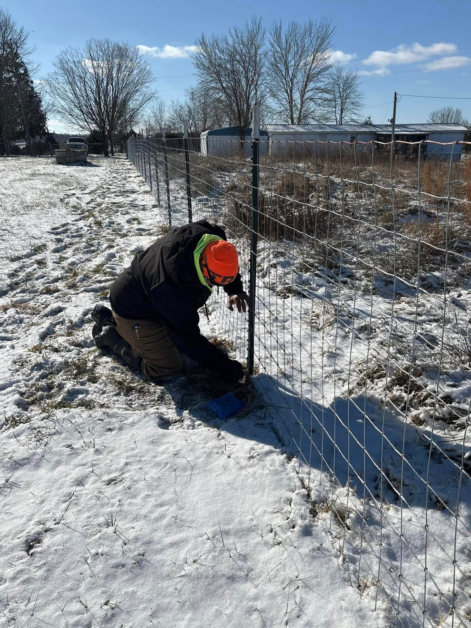 A man is working on a fence in the snow.