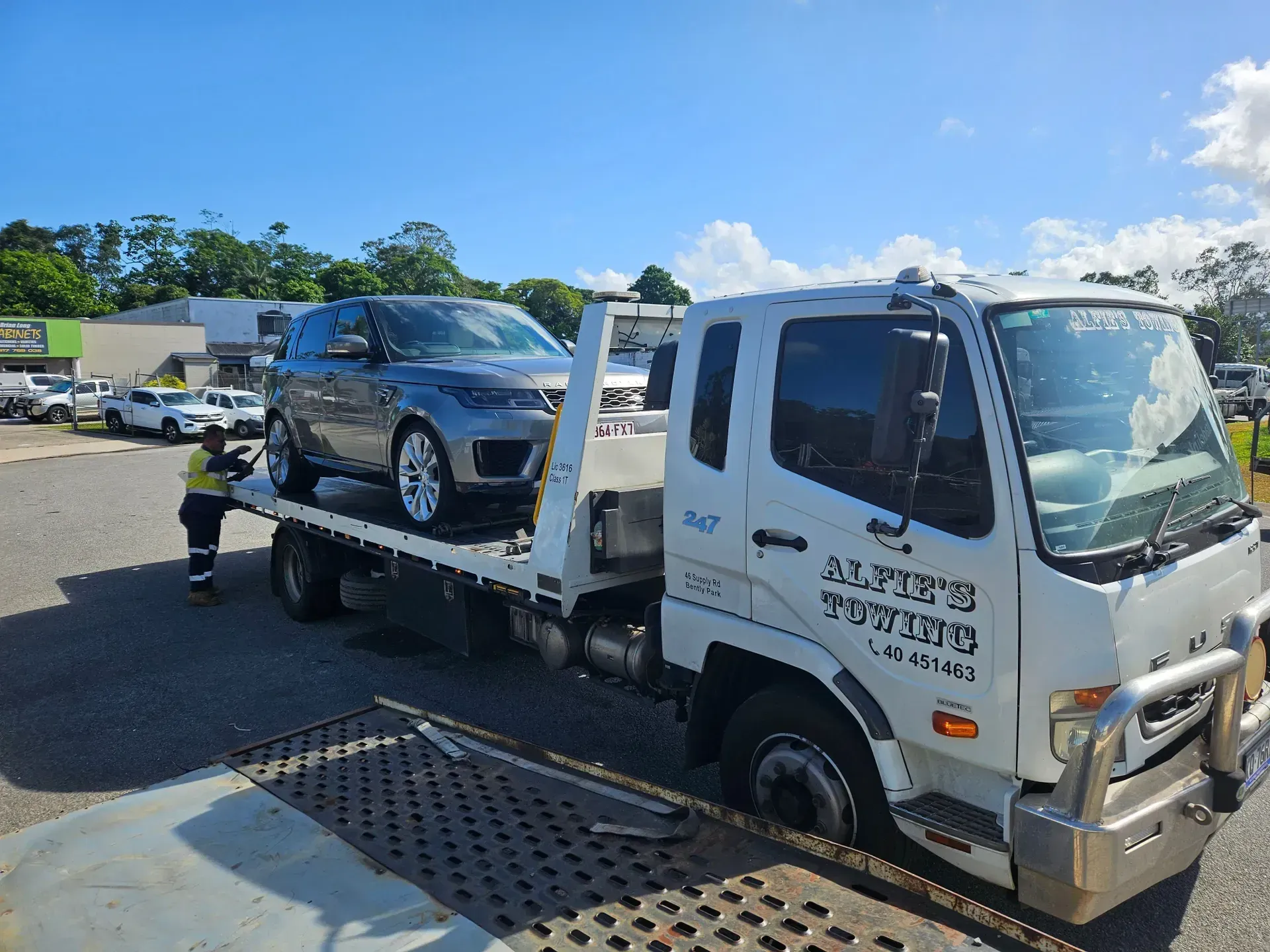 Grey Suv Being Loaded Onto a White Tow Truck by a Worker on a Sunny Day — Alfie's Towing in Malanda, QLD