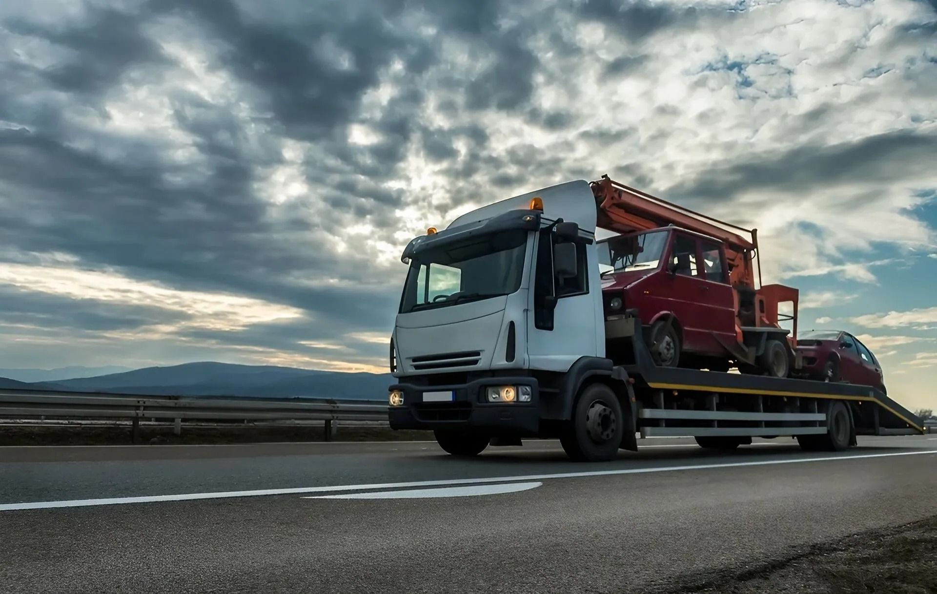 Tow truck carrying a red car on a highway under a cloudy sky — Alfie's Towing in Normanton, QLD