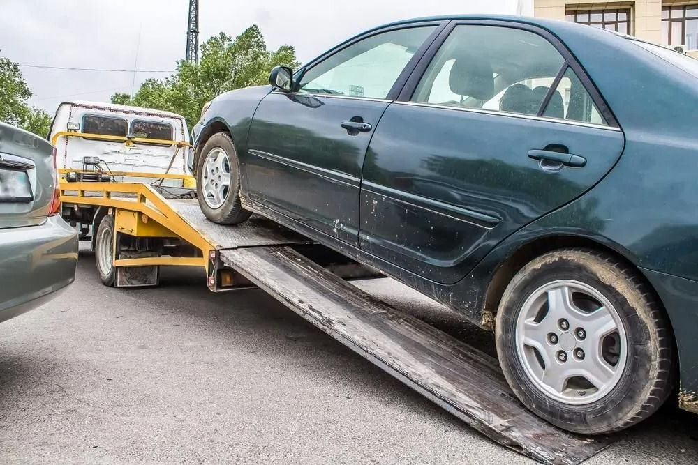 Green Sedan Being Loaded Onto a Yellow Tow Truck on a Paved Surface — Alfie's Towing in Georgetown, QLD