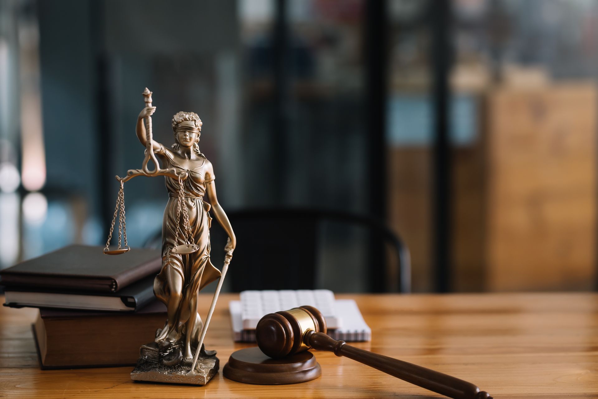 Statue of Lady Justice with scales, books, and a gavel on a wooden table.
