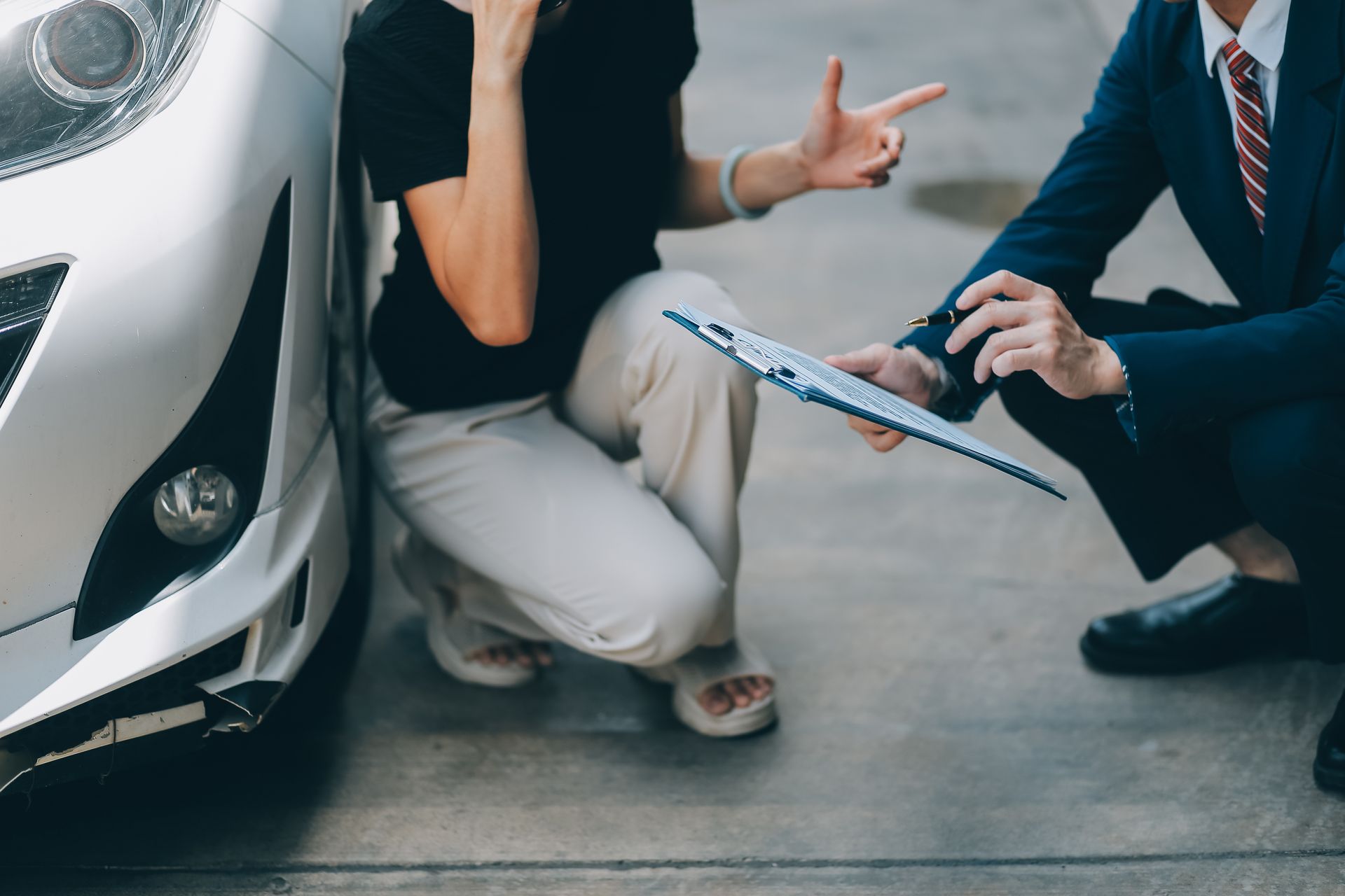 Woman gesturing with hands near a damaged car, discussing with a man in a suit.