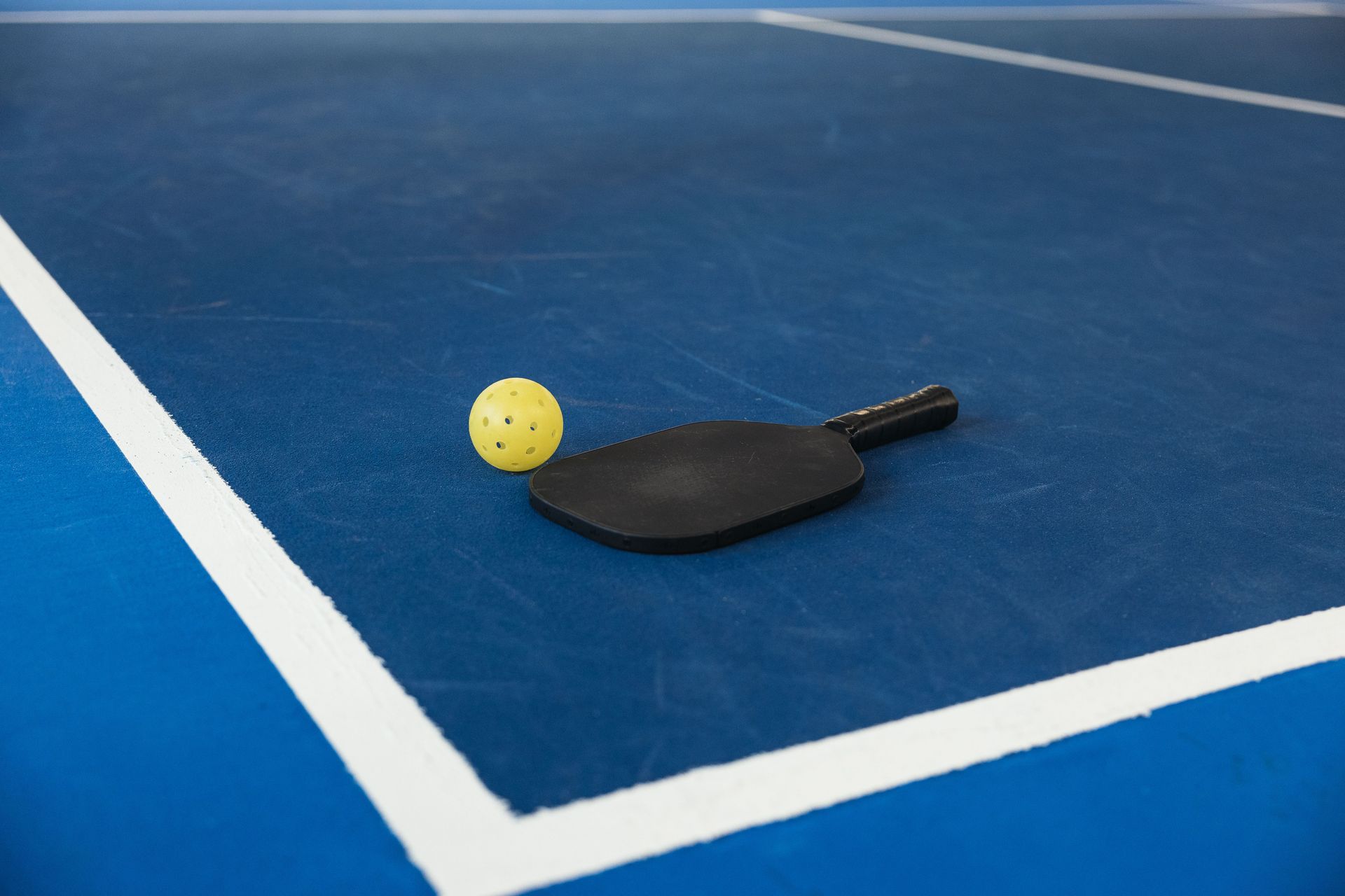 Pickleball paddle and yellow ball on a blue court