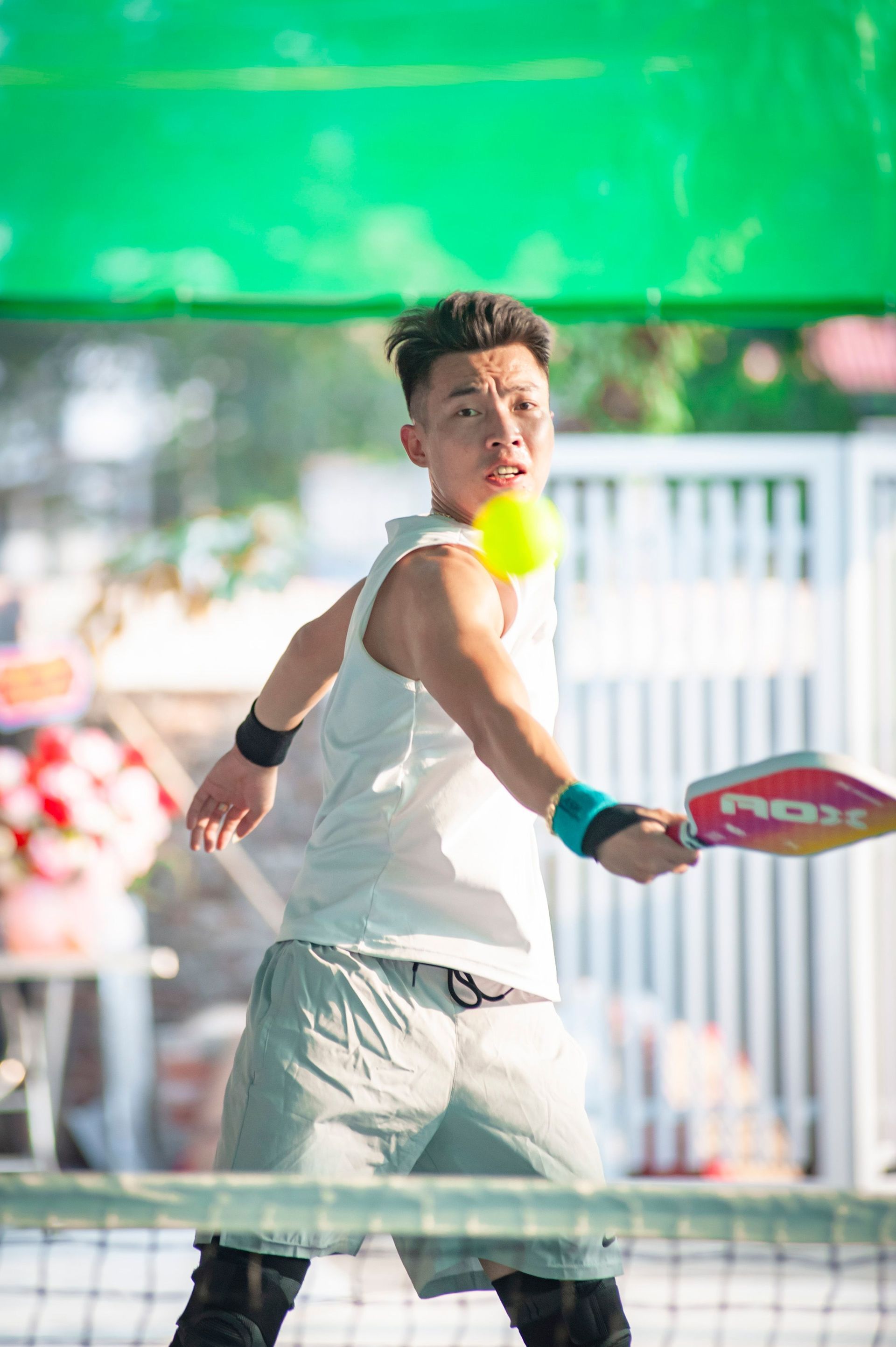 pickle player in white shirt and shorts hitting a ball on an outdoor court