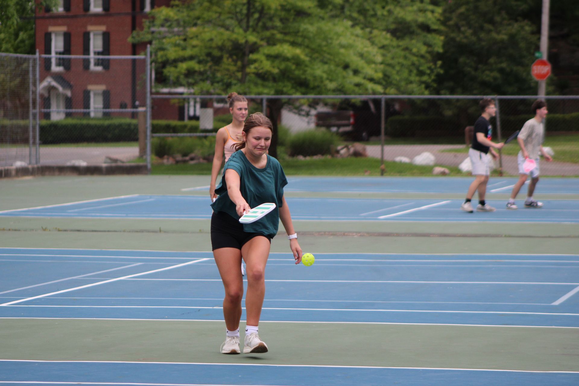 Two tennis players on a blue court, one in front holding a racket and ball, with others in the background.