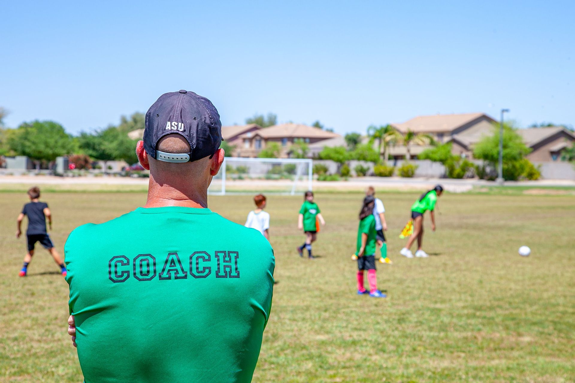 Coach in green shirt watching children practice soccer on a sunny field