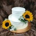 A white wedding cake with sunflowers on top of it.