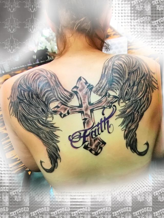 A woman has a tattoo of a cross and wings on her back.