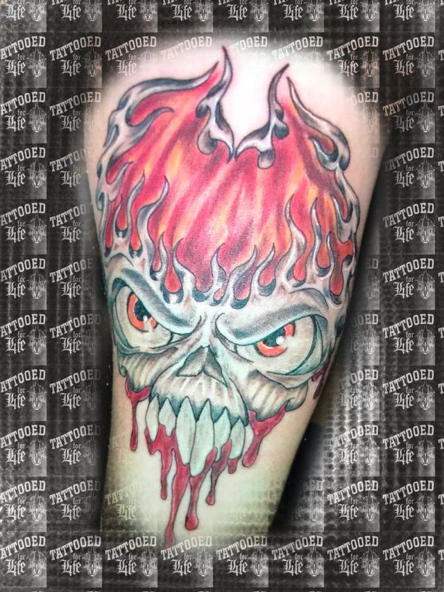 A tattoo of a skull with flames coming out of it