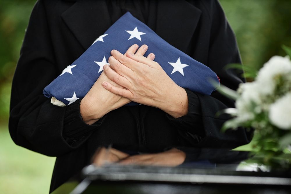 A woman is holding an american flag and a rose at a funeral.