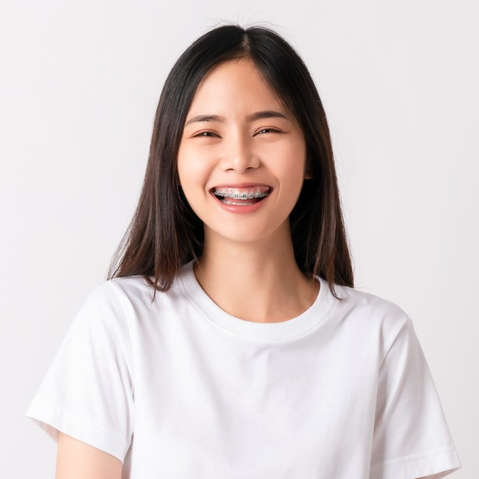 A smiling person with dark hair, wearing a white t-shirt and dental braces, against a plain white background.