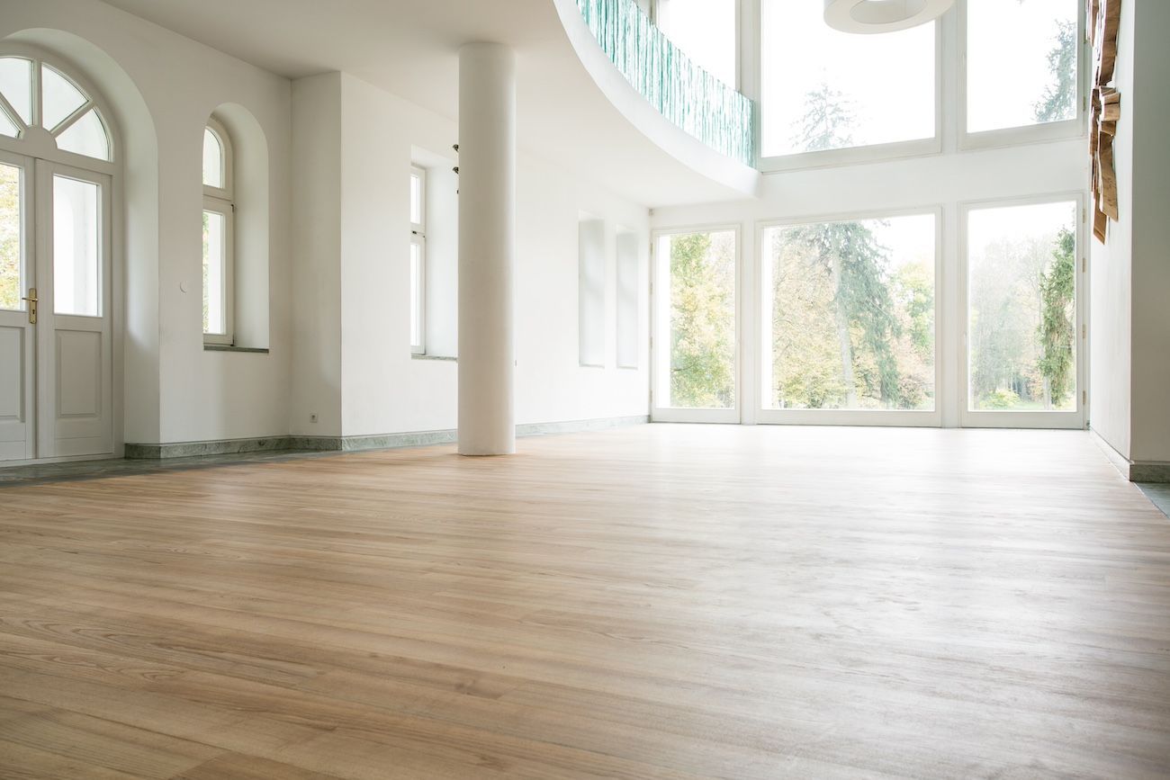Chambre spacieuse et lumineuse avec parquet, murs blancs et grandes fenêtres donnant sur une forêt.
