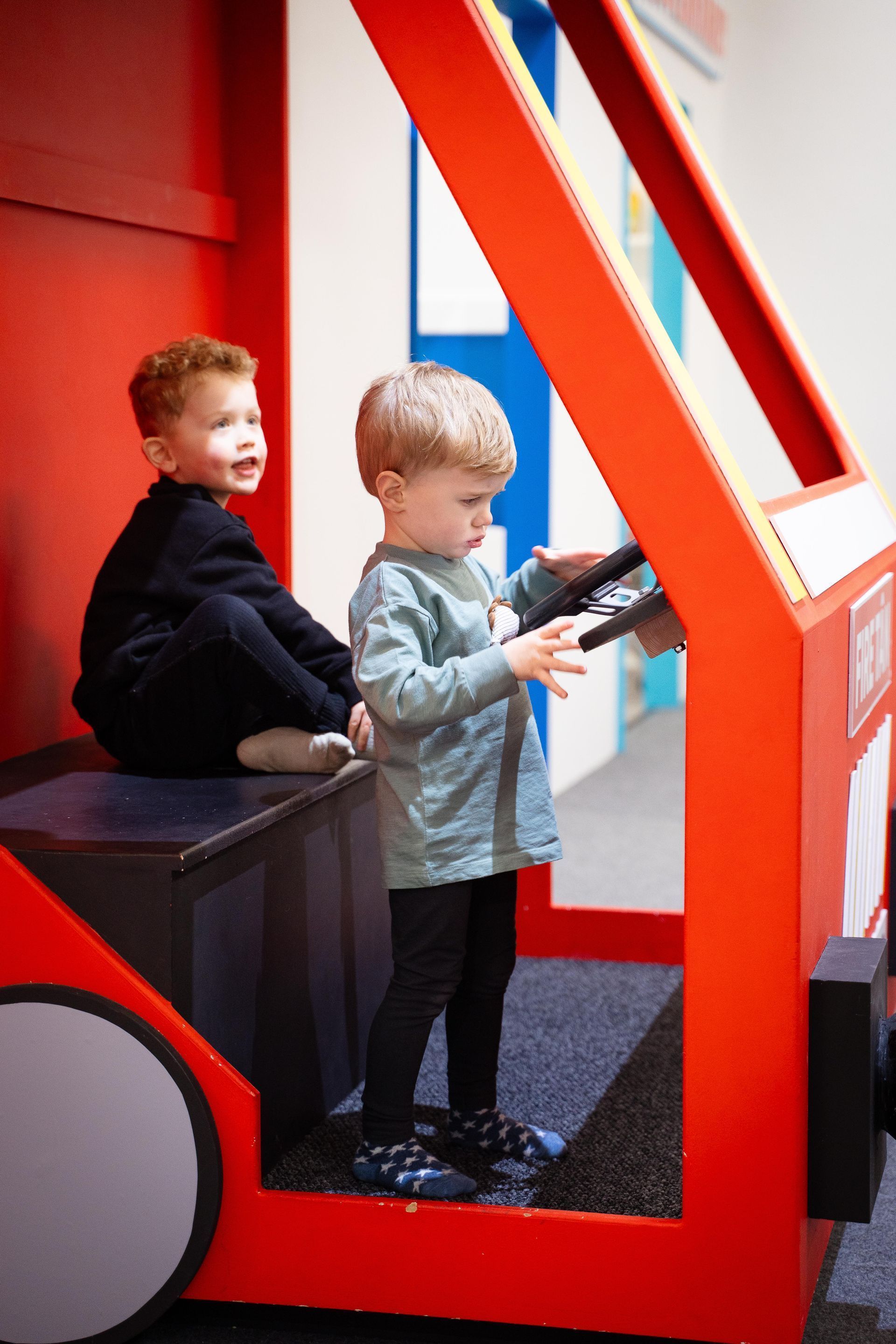 Two young boys are playing in a toy fire truck.