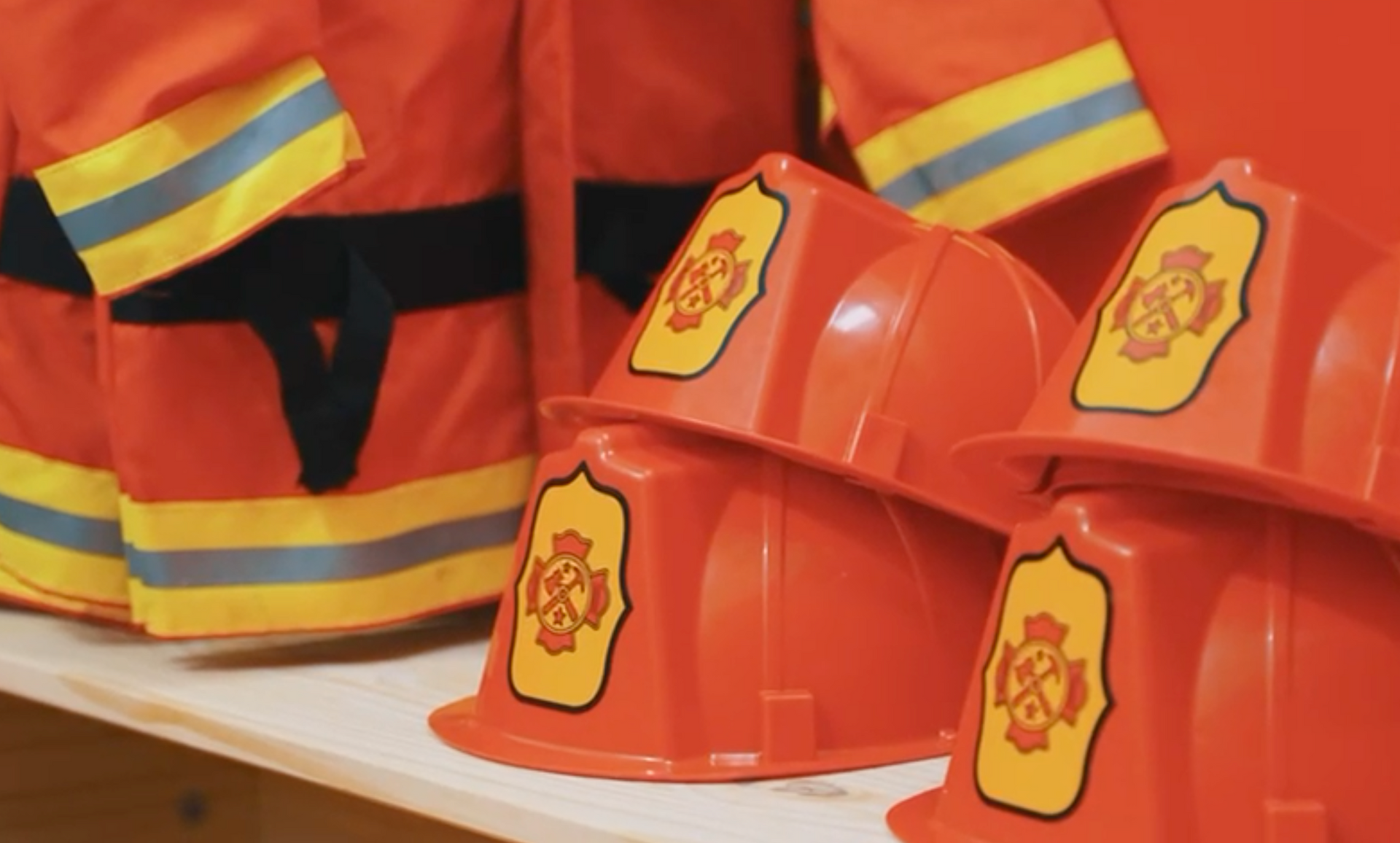 A row of firefighter helmets and uniforms on a shelf.