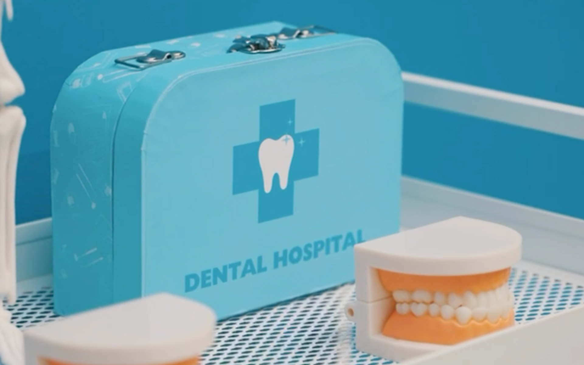 A blue dental hospital suitcase is sitting on a tray next to a tooth model.