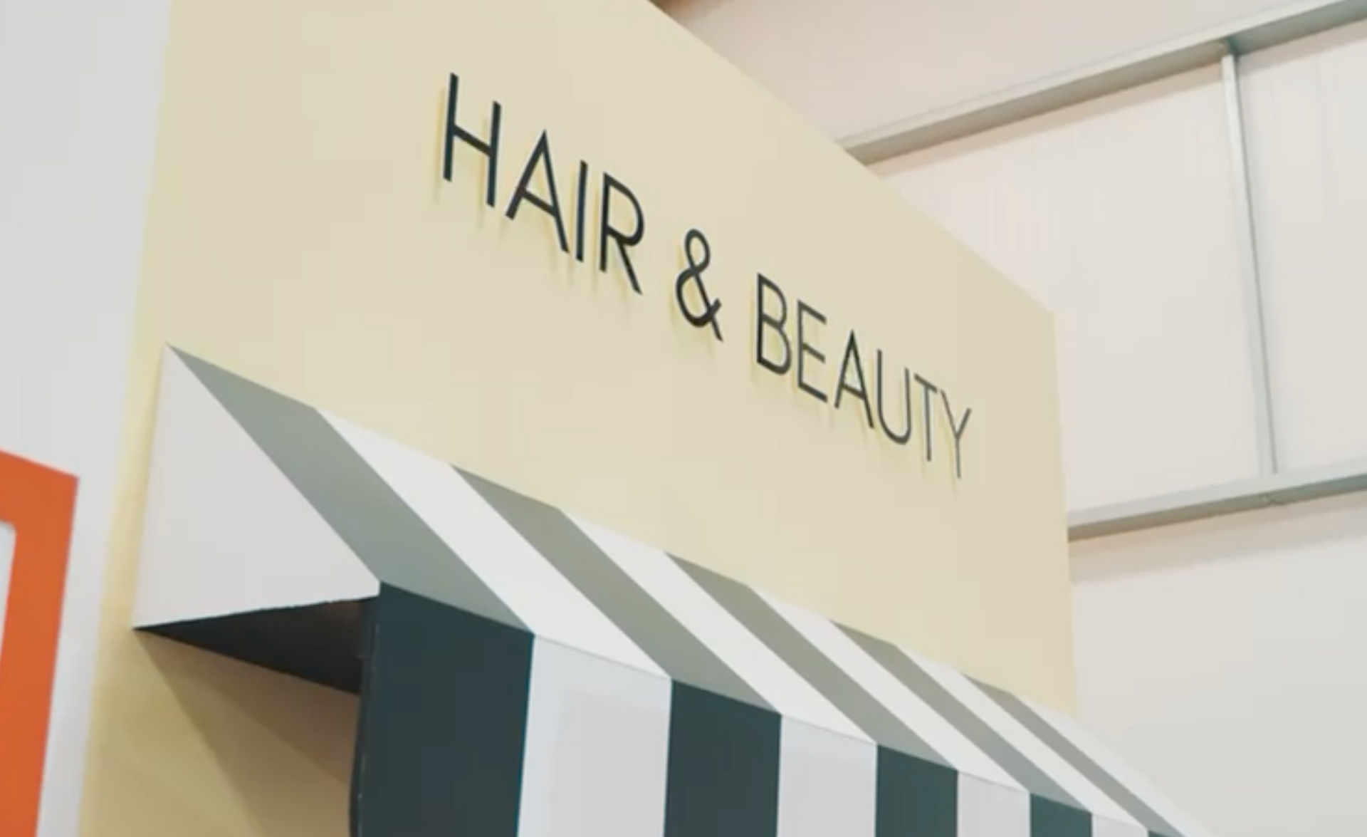A sign for a hair and beauty salon with a striped awning.