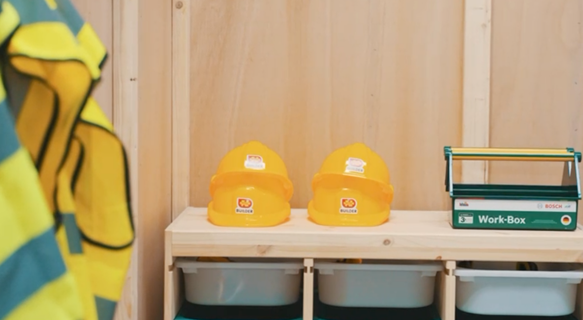Two yellow hard hats are sitting on a wooden shelf next to a work box.