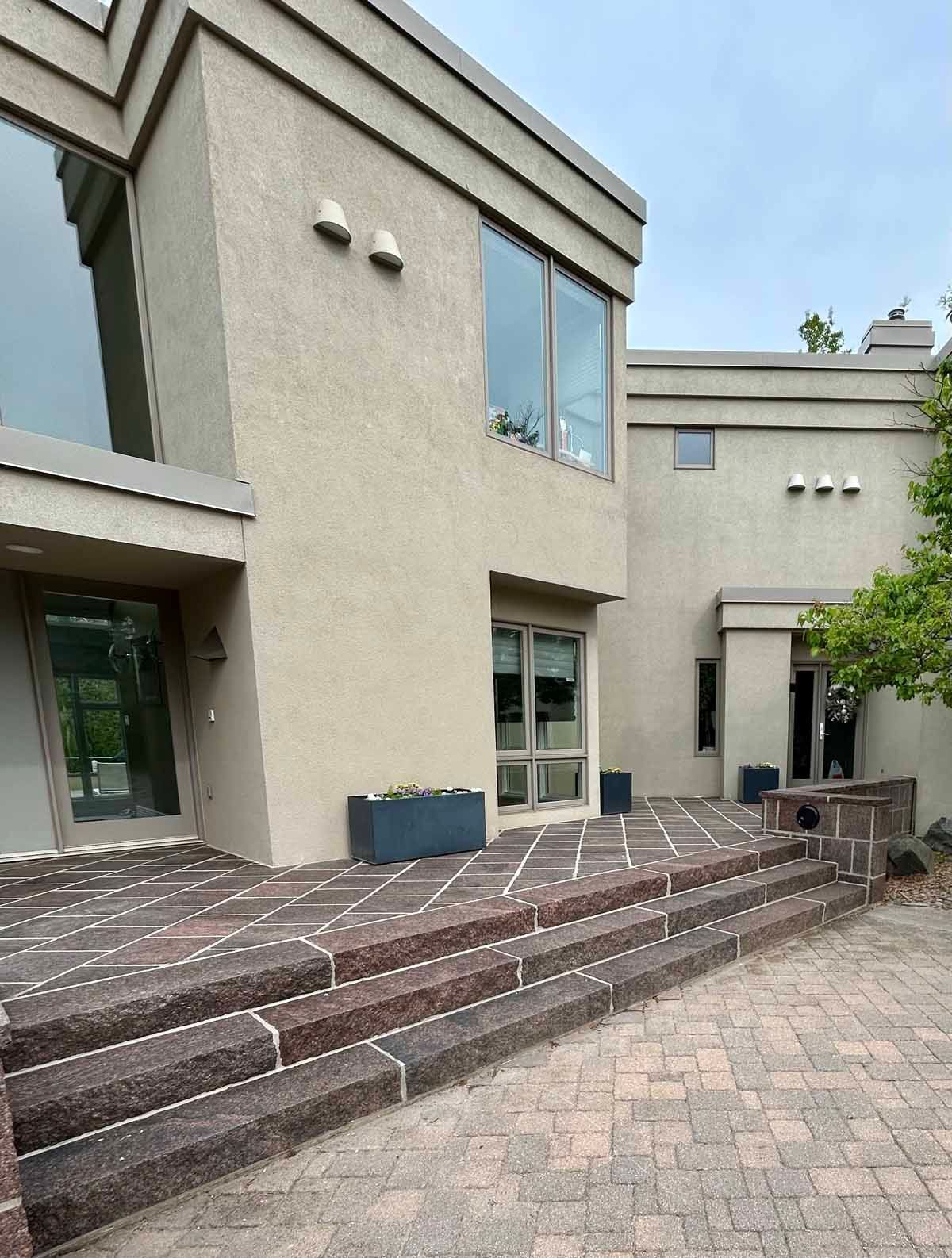 Beige stucco house with brick steps and walkways. Large windows, dark planters, and a cloudy sky.