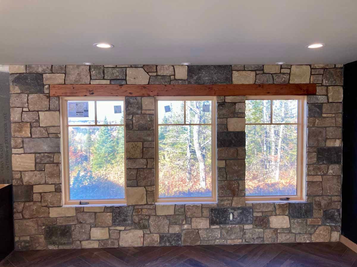 Three windows set in a stone wall with a wooden header. Trees visible outside.