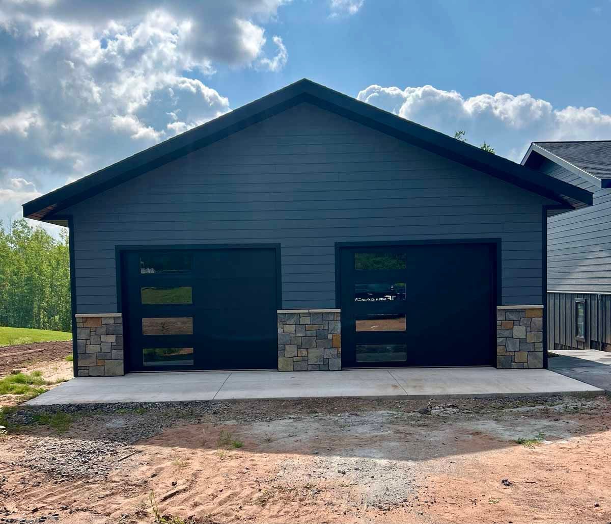 Two-car garage with black doors and stone accents, blue-gray siding, and a concrete driveway.