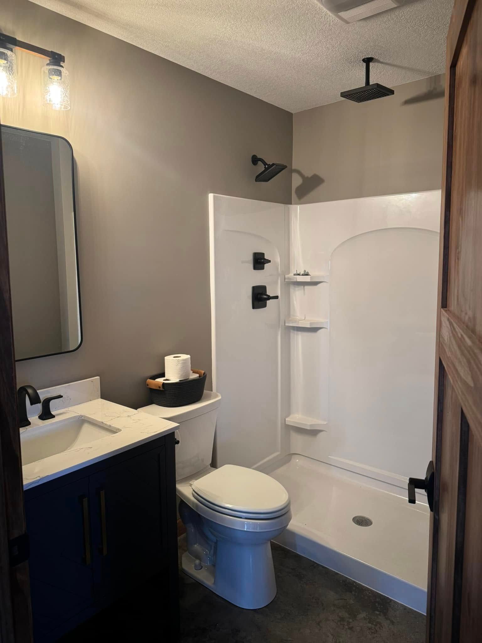 A bathroom with a toilet , sink , shower and mirror.