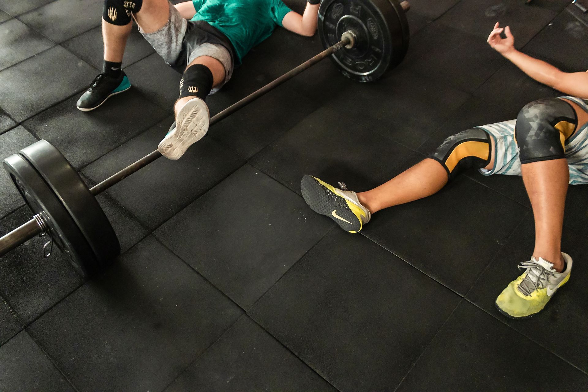 People lying on a gym floor beside a barbell with weight plates