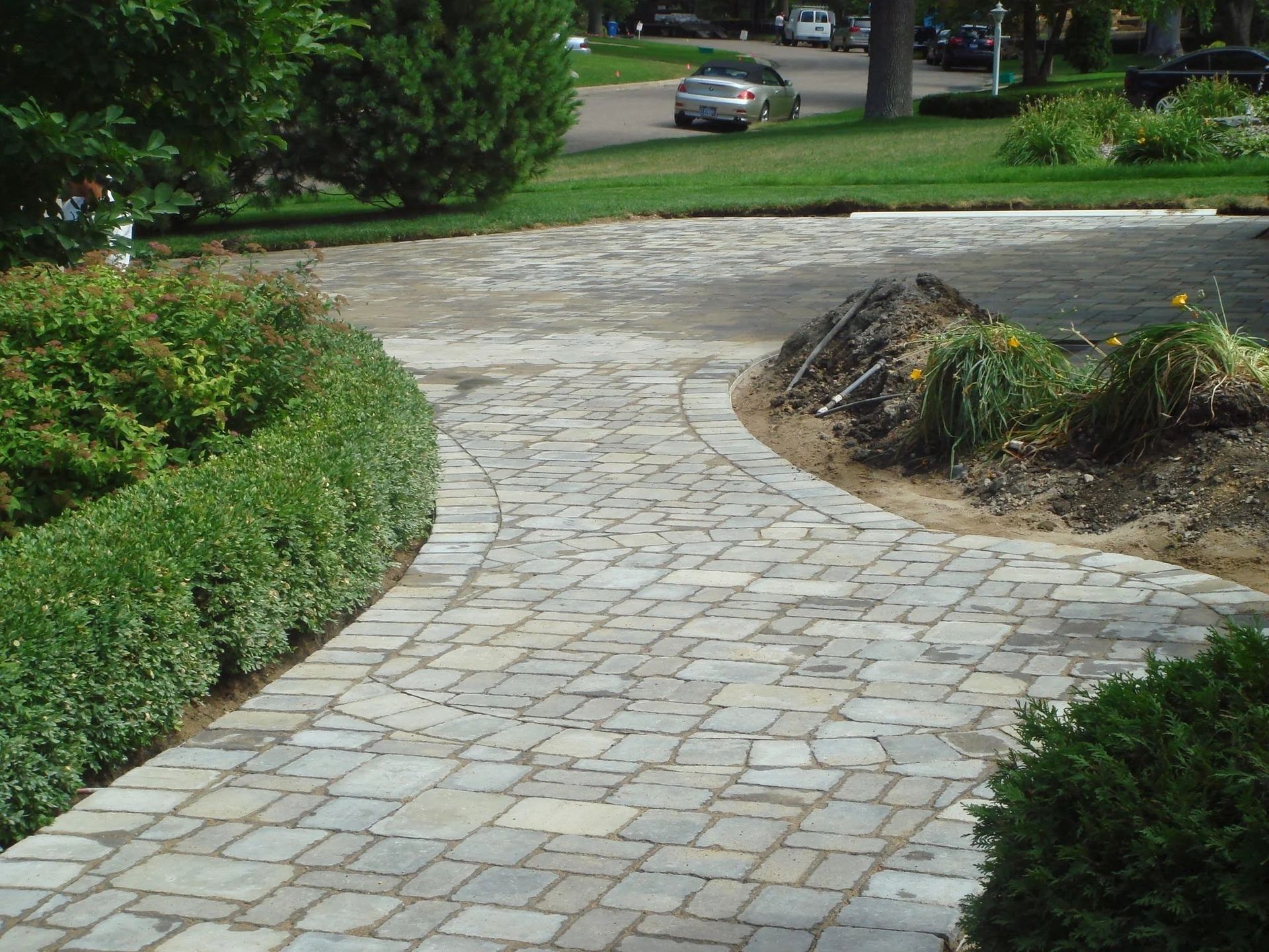 Curved stone walkway bordered by green shrubs in a landscaped yard