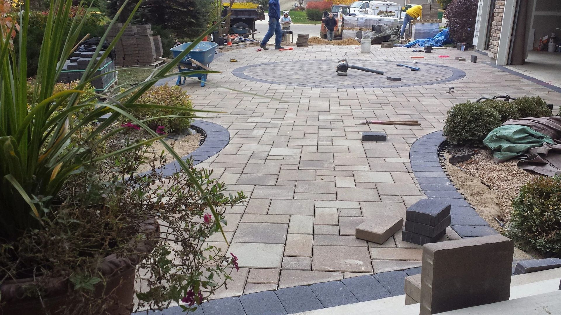 Partially paved walkway under construction, with scattered bricks, tools, and workers in the distance.