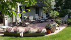 Patio garden with potted flowers, lounge chairs, and a small table beside a house