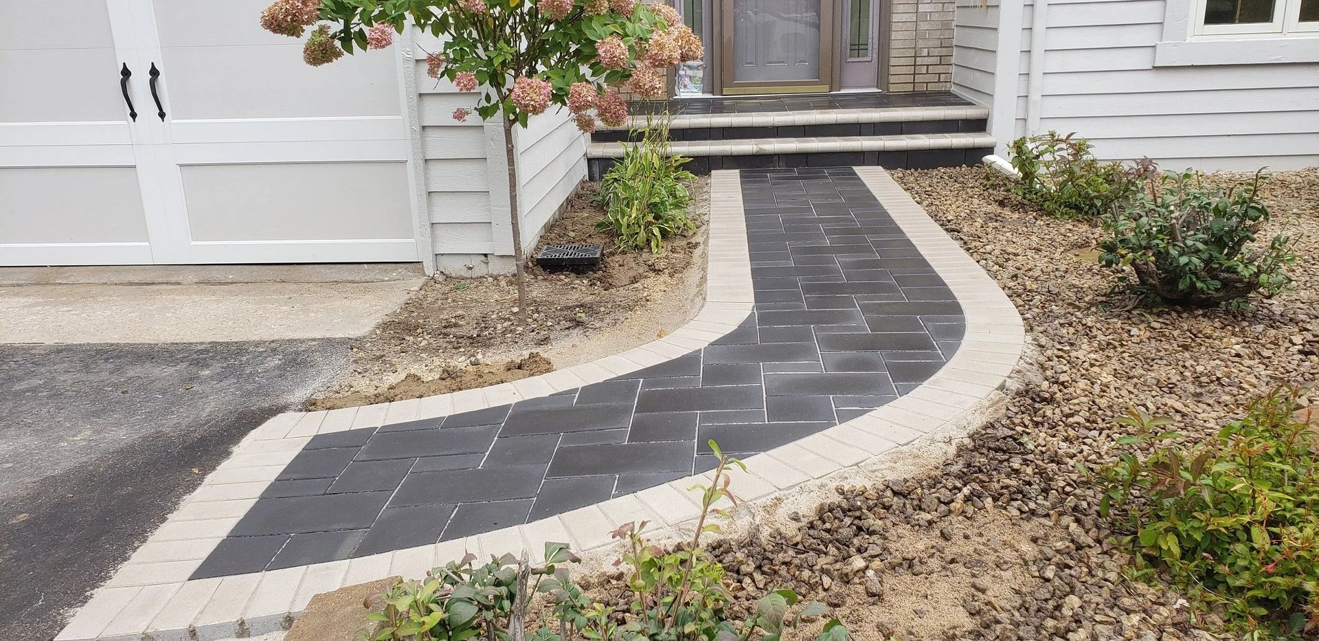 Curved dark stone walkway leading to a front door, bordered by gravel and plants