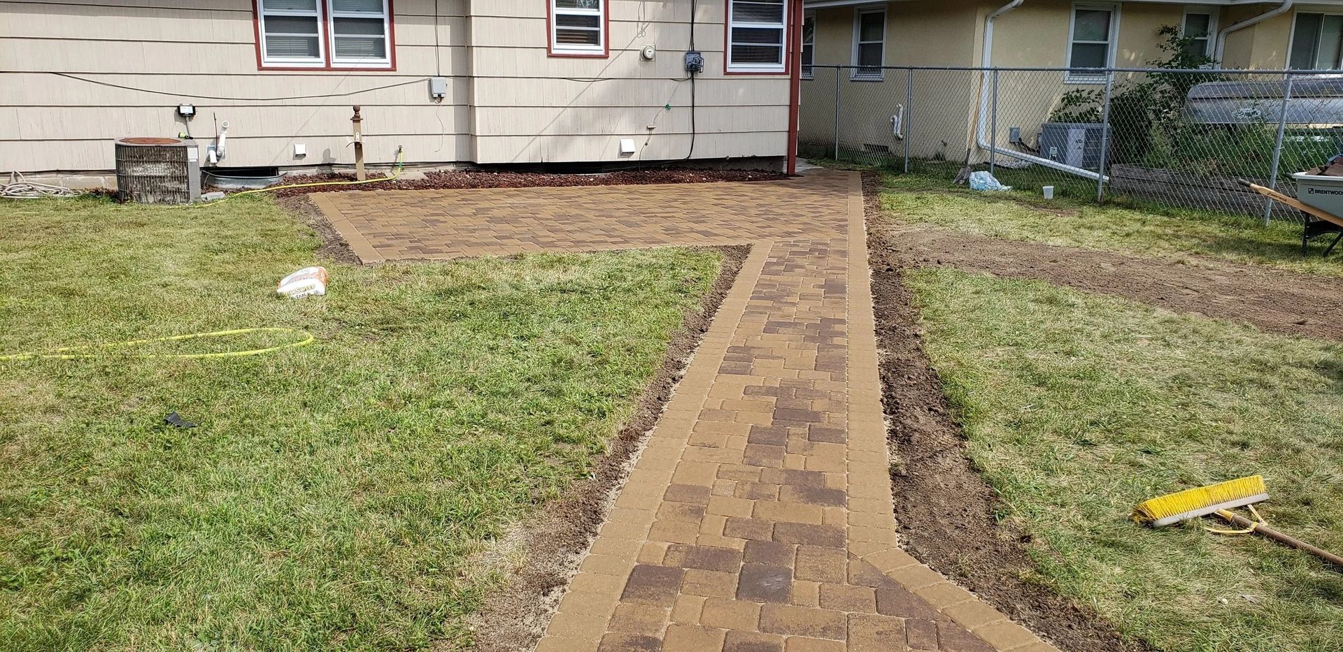 Brick walkway leading to a beige house across a grassy yard.