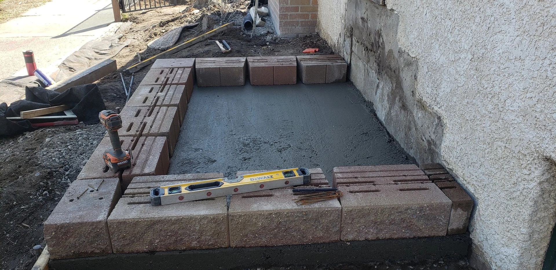 Construction site with a small brick-lined foundation filled with gravel beside a stucco wall.