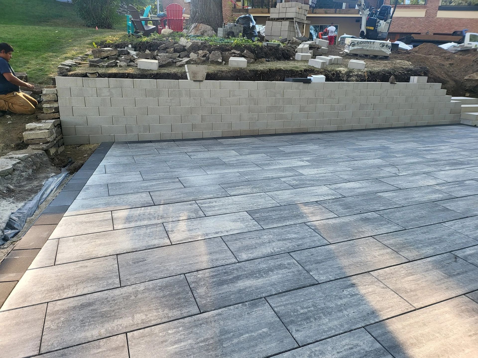 Stone patio in front of a raised retaining wall and garden bed, with two people at the left edge.