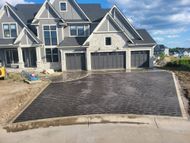 Newly paved dark driveway in front of a large gray house with three garage doors