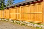 Wooden privacy fence with stone base along a gravel yard, lit by sunlight.