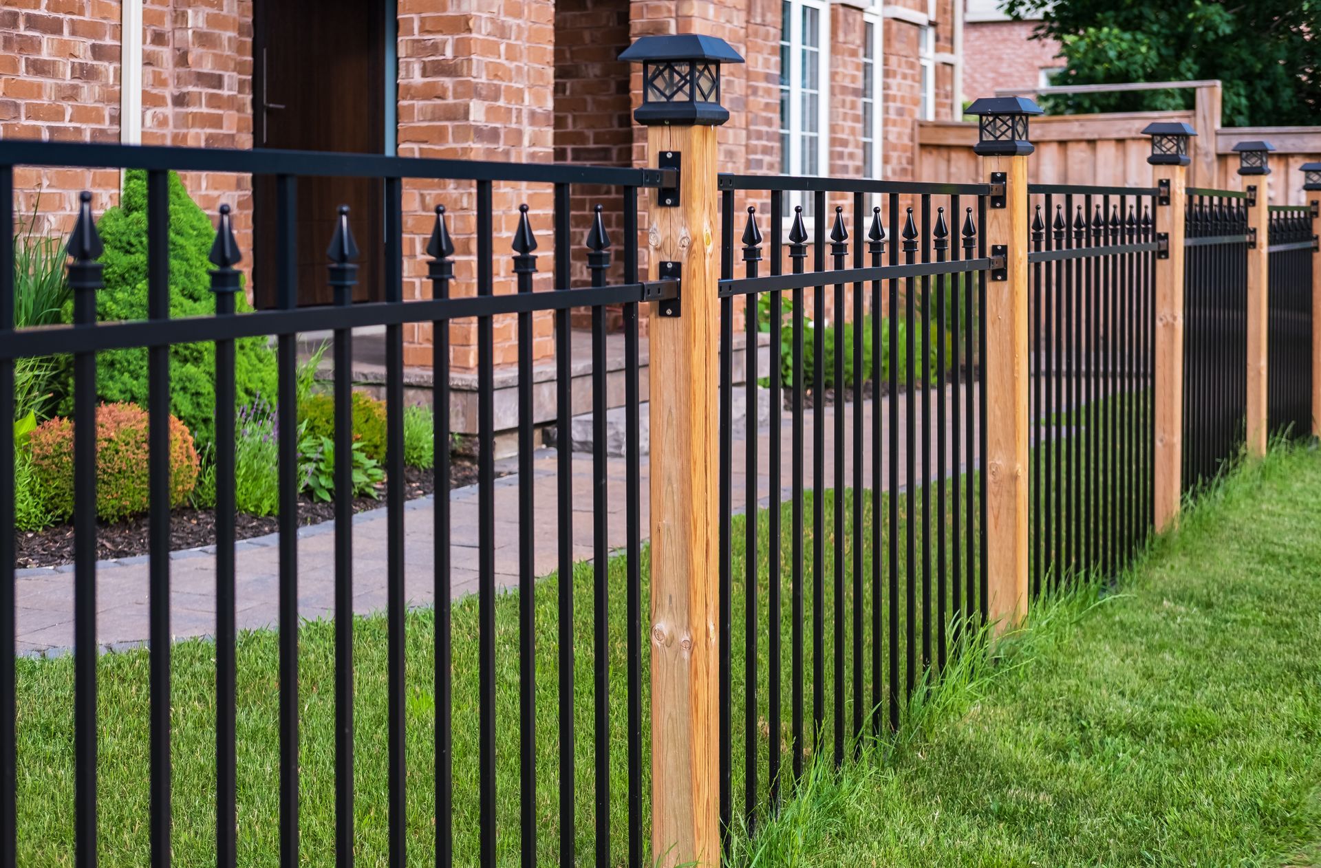 Black metal fence with wooden posts along a brick house and green lawn
