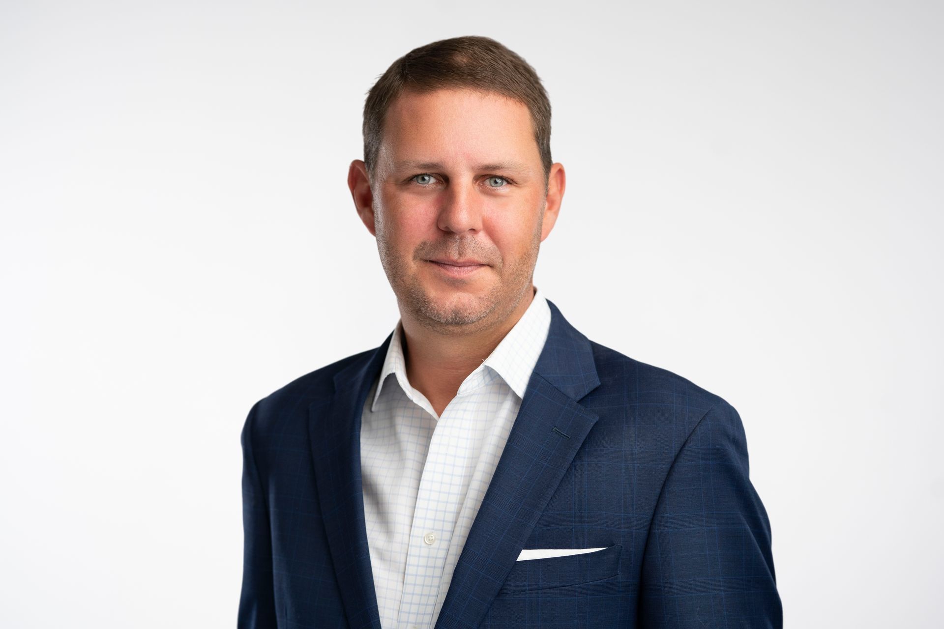 A man in a blue suit and white shirt is standing in front of a white background.
