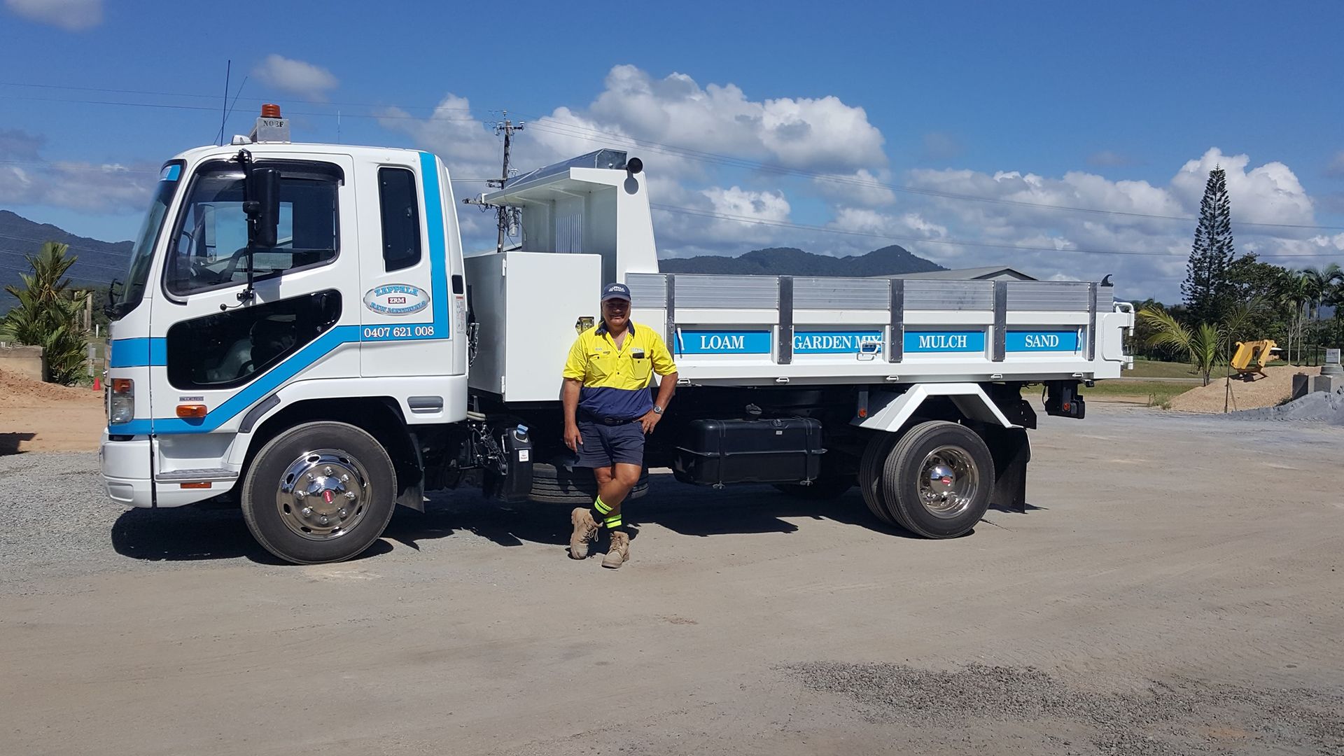A Man Is Standing Next To A Dump Truck In A Parking Lot — Zappala Raw Materials Pty Ltd In Edmonton, QLD