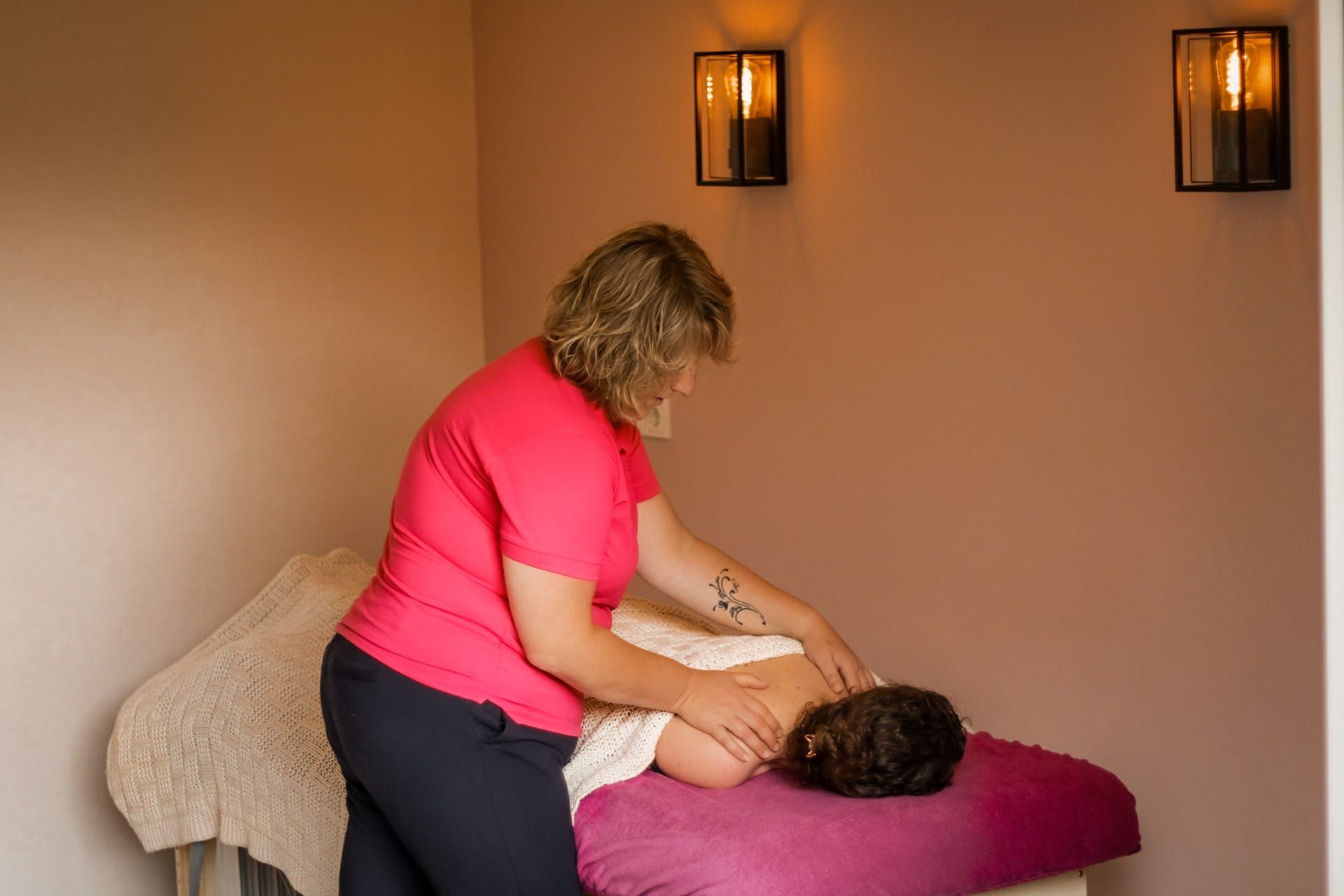 Een massagetherapeut behandelt een cliënt op een massagetafel in een sfeervol verlichte ruimte.