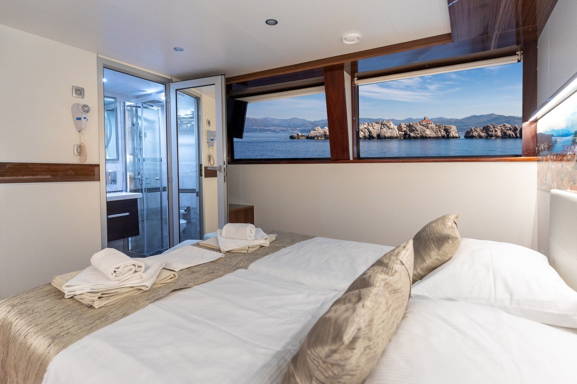 Bedroom on a boat with a bed, windows with sea view, and a bathroom visible.