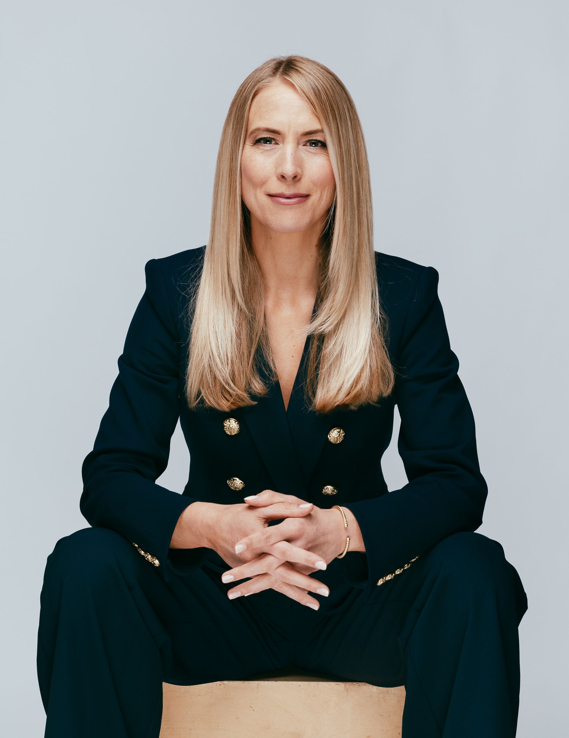 Sam Johnson in a suit is sitting on a box with her hands folded.