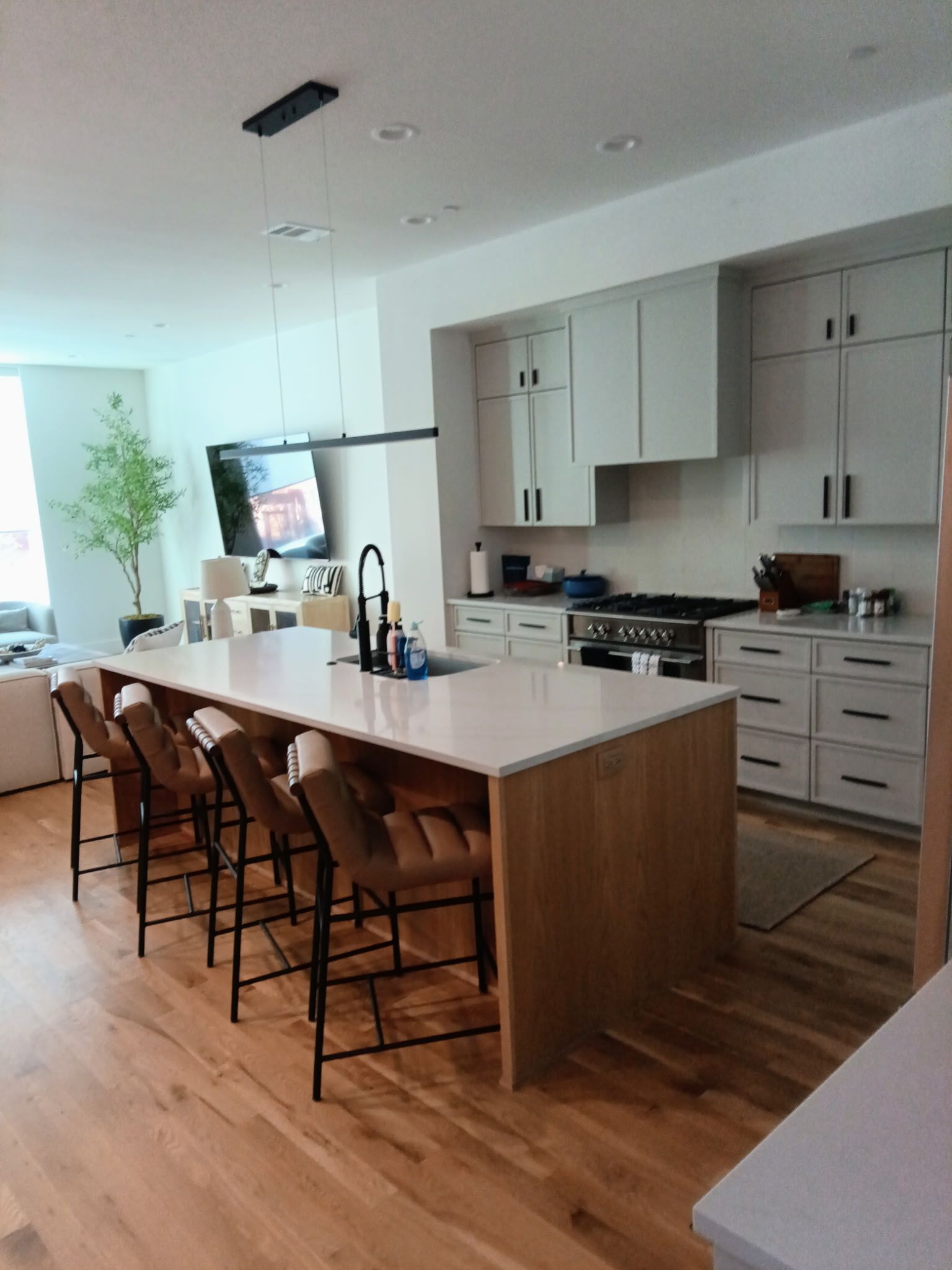 Modern kitchen with light wood floor, white cabinets, island with stools, and TV.
