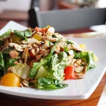 A salad with lettuce tomatoes and almonds on a white plate