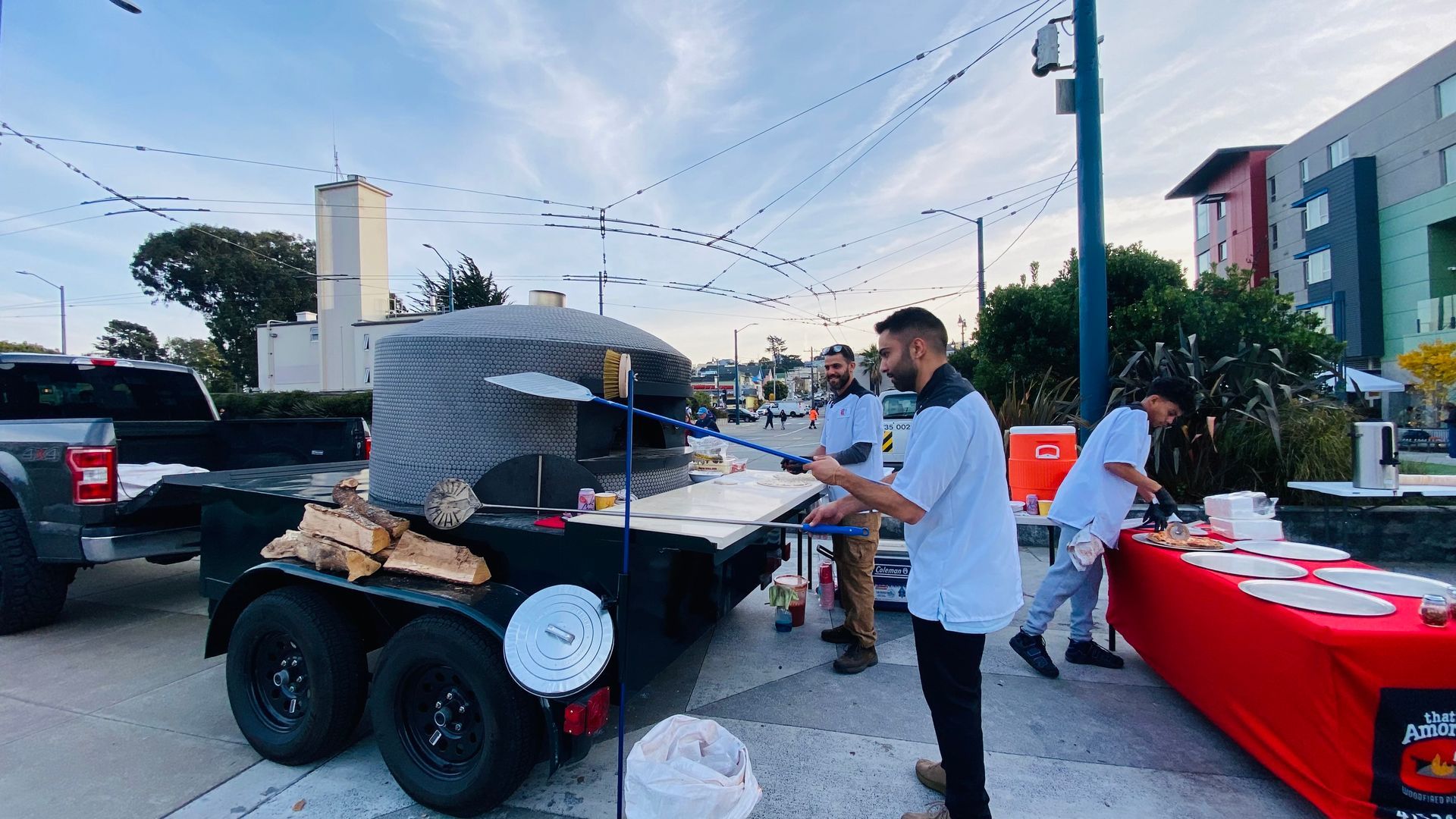A group of men are standing in front of a pizza oven on a trailer.
