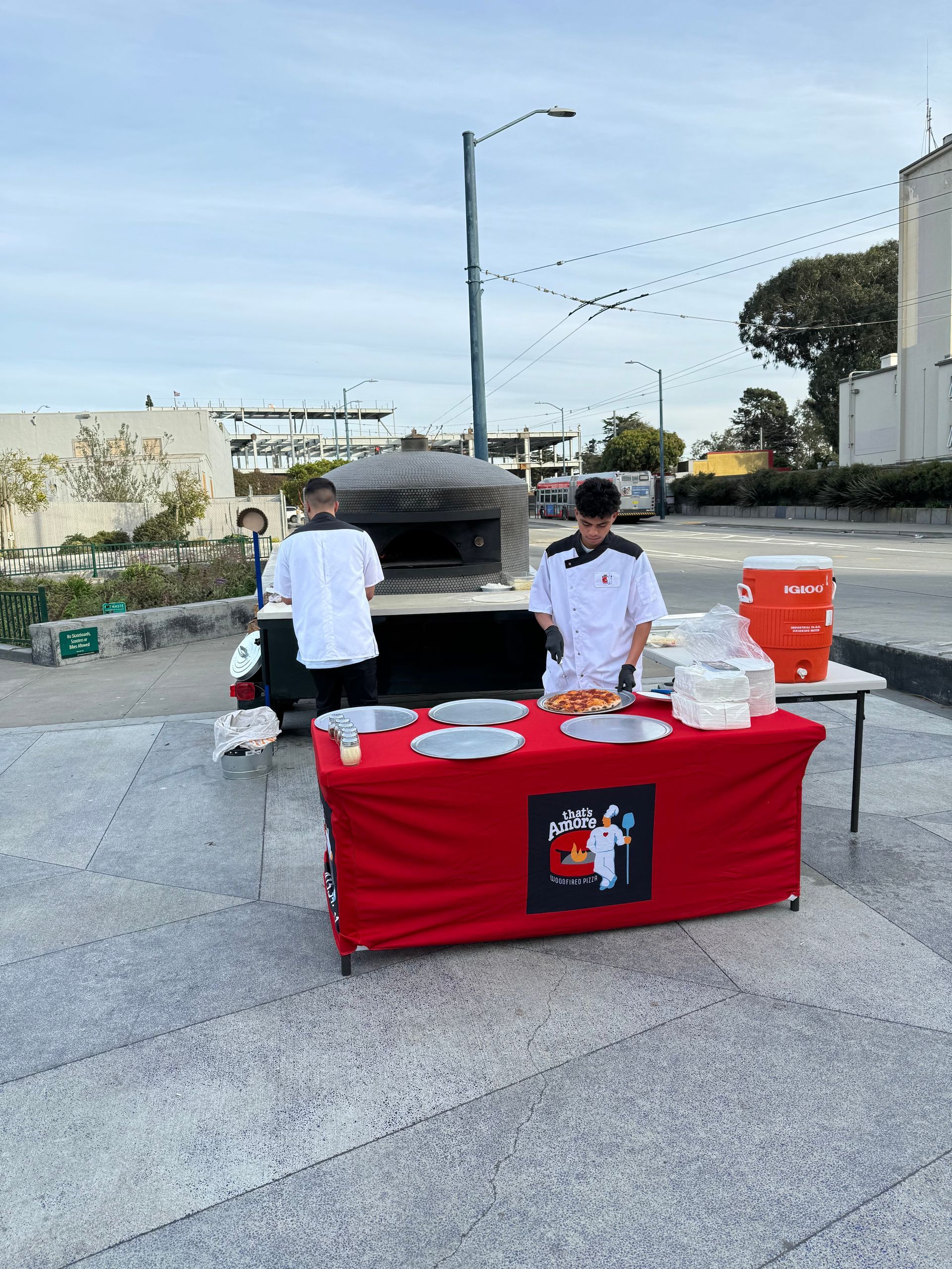 A man is standing behind a table with plates on it in front of a pizza oven.