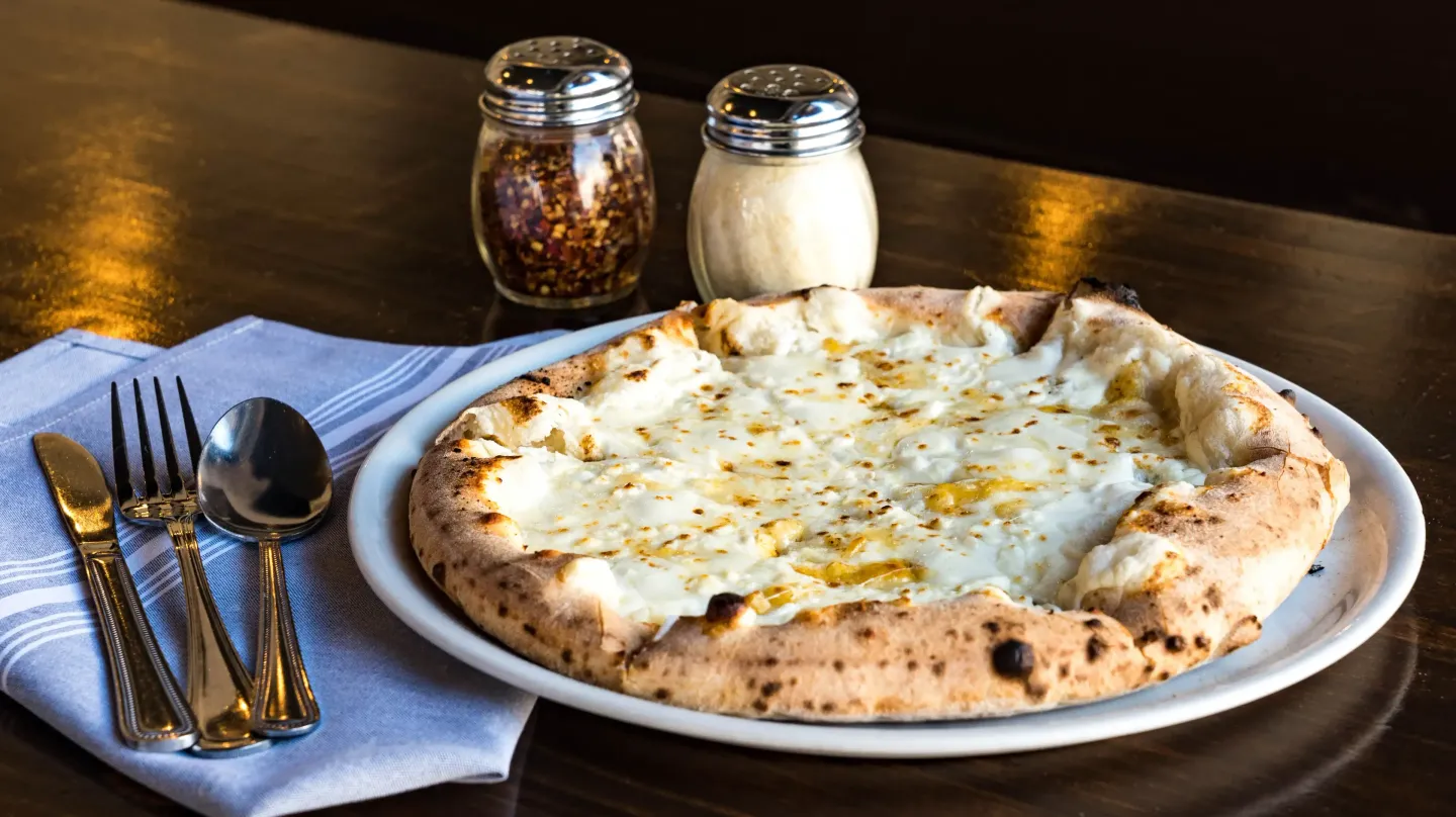 A pizza on a plate with utensils on a table.