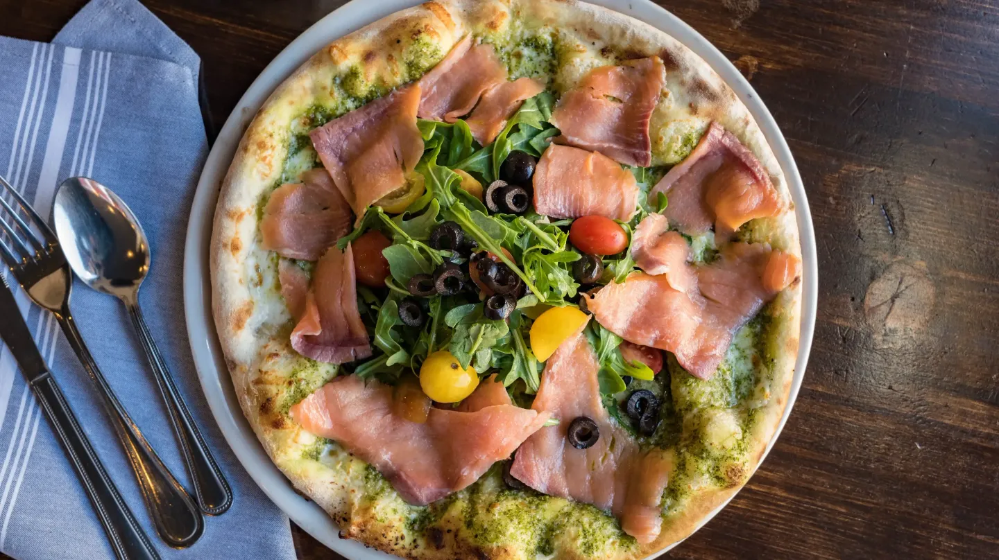 A pizza with a salad on top of it is on a plate on a table.